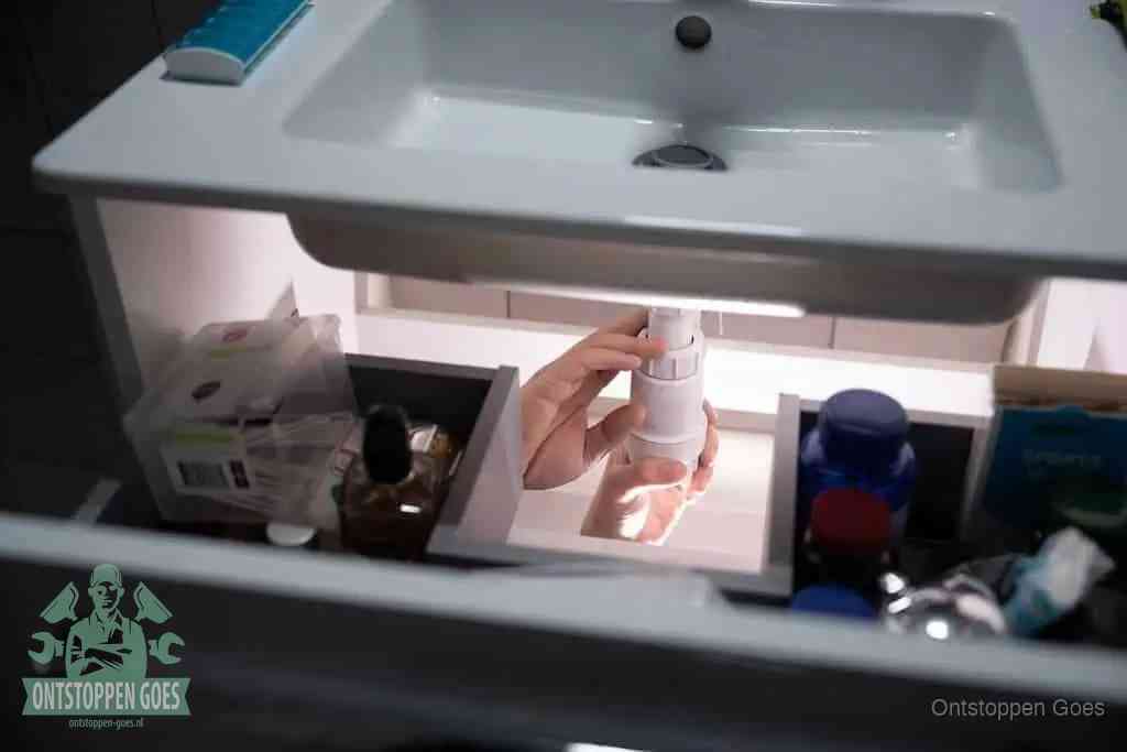 Een pompfles met zeep boven een wastafel, de heet water en afwasmiddel-methode om een vetprop in de afvoer los te maken in Goes