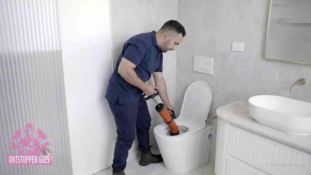 Een monteur buigt over een wandcloset en duwt met de hand een persluchtontstopper in de toiletpot om de verstopping handmatig los te maken in Goes