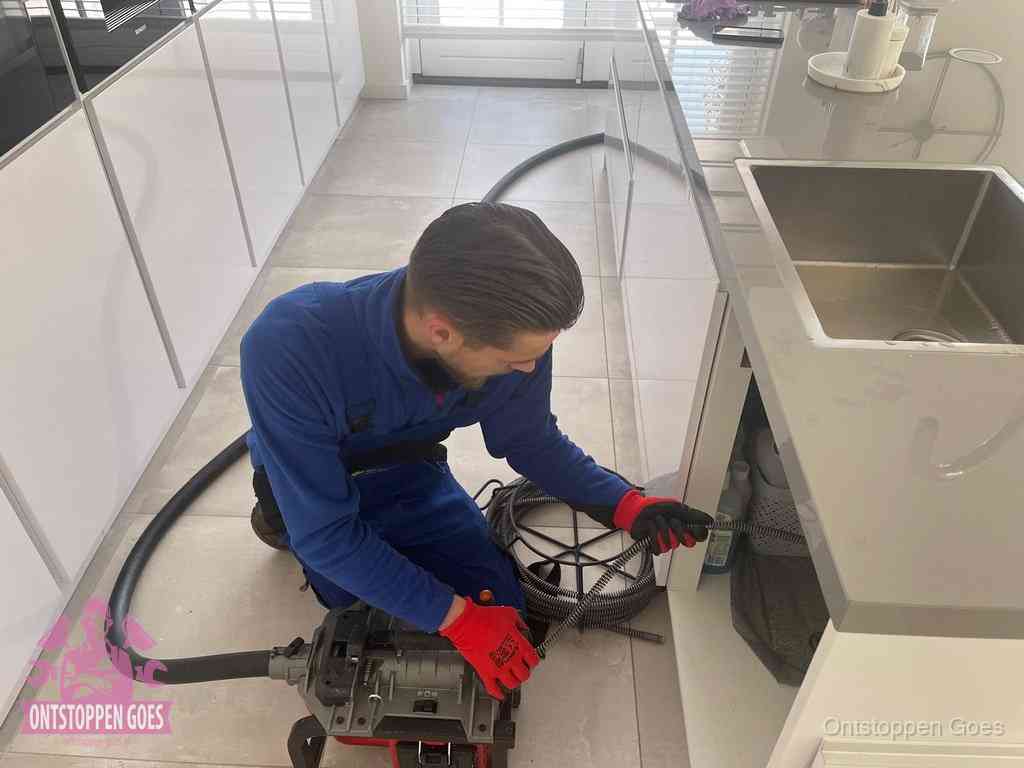 Een monteur ontstopt de keukenafvoer onder de spoelbak met een elektrische veermachine in Goes