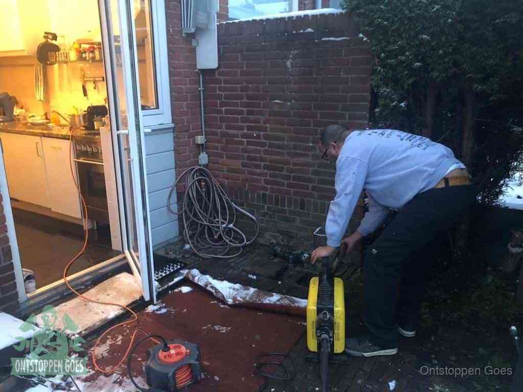 Een monteur werkt buiten bij een open riool-/grondput met een elektrische ontstoppingsmachine om een verborgen afvoerprobleem op te sporen in Goes