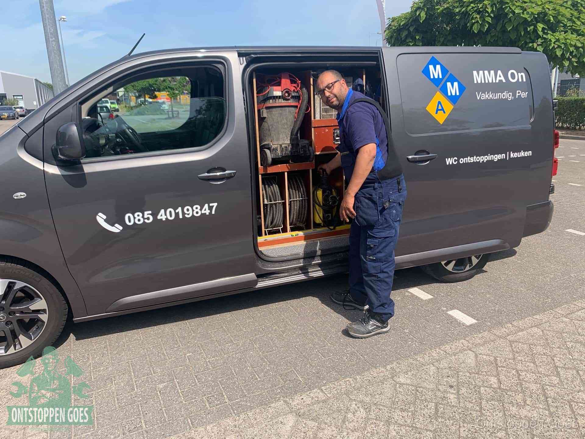 Een monteur bij de open schuifdeur van zijn bedrijfsbus op een parkeerplaats, klaar om de oorzaak van terugkerende afvoerverstoppingen aan te pakken in Goes