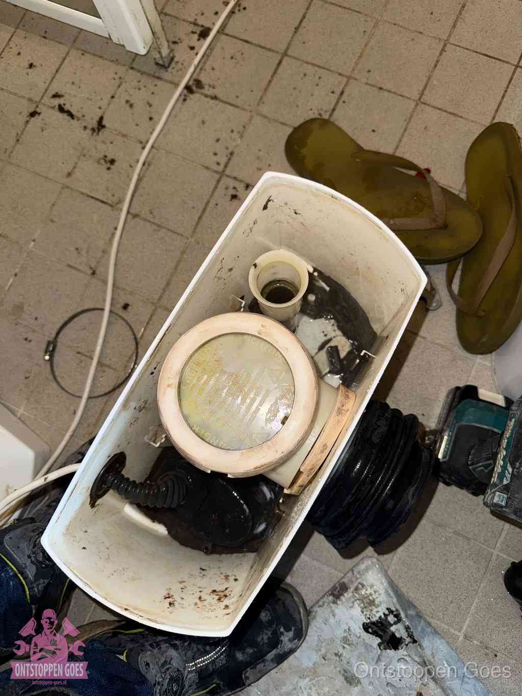 Een gedemonteerde toiletpot op de vloer met ontstoppingsveer en gereedschap ernaast, het verwijderen van een vastzittend voorwerp uit de wc in Goes