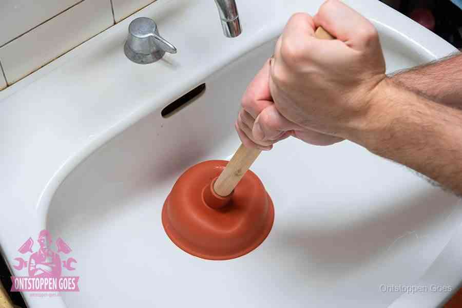 Twee handen gebruiken een rode rubberen plopper op een sanitair-afvoer om het toilet te ontstoppen in Goes