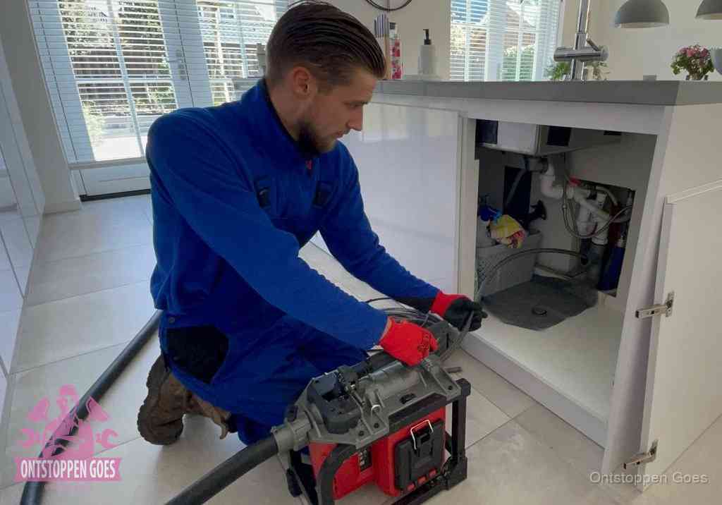 Een monteur voert een professionele elektrische ontstoppingsmachine in de afvoer onder de spoelbak tijdens het gootsteen ontstoppen in Goes