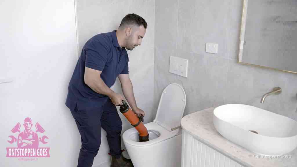 Een man gebruikt een handmatige luchtdruk-ontstopper in een modern betegeld toilet om zelf de wc te ontstoppen in Goes